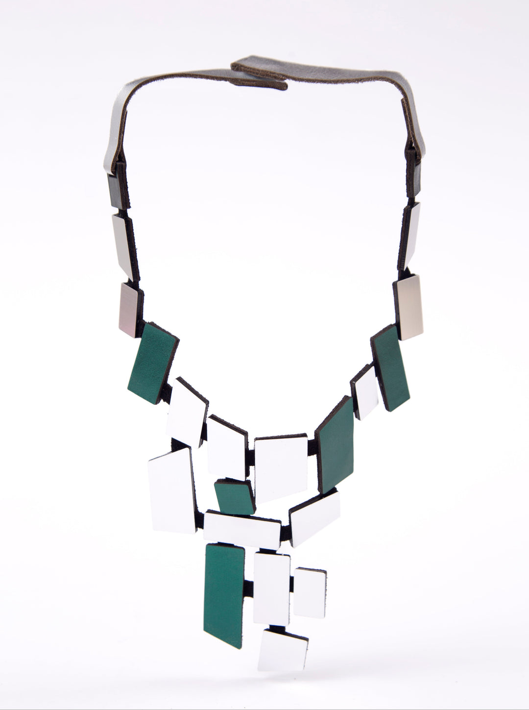 The Piet Green & Silver Necklace by Iskin Sisters features irregular green and white tiles in a geometric, abstract design with a black frame and leather-like strap—ideal for fans of modern art jewelry. Shown on a white background.
