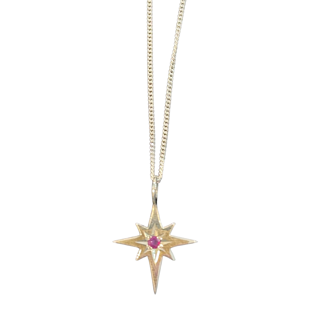 The Cosmic Boulevard Polaris Ruby & Sterling Silver Pendant features a gold star-shaped design with a central pink gemstone, shown against a white background.
