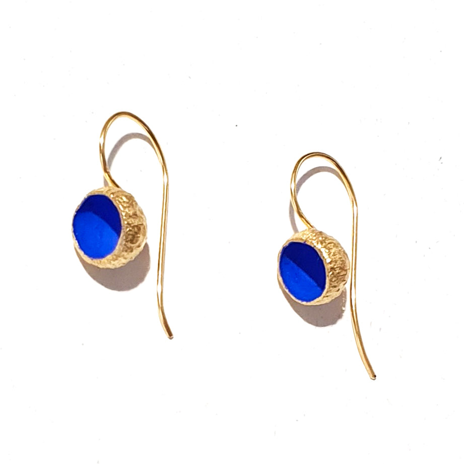 A close-up image of a pair of Acorn Cup Matt Drop Earrings by Georgia Charal. Each earring features a hook design with a round blue stone set in a textured, gold-plated bezel. The plain white background accentuates the vibrant blue and gold colors of the elegant, handmade earrings.