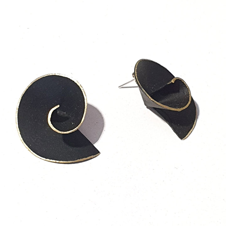 A pair of black, handmade Matt Swirl Earrings by Georgia Charal with gold plated silver edges on a white background. One earring lies flat, showcasing its coiled design, while the other stands upright, revealing the metallic stud.