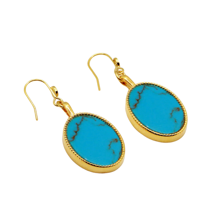 The Frida Earrings by Nilai feature 24K gold-finished hooks and oval-shaped turquoise gemstones with delicate brown veining patterns. Handmade in Paris, these elegant earrings are photographed against a white background.