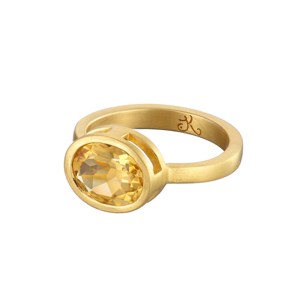 A Citrine Pirate Ring In Silver featuring an oval-cut citrine gemstone set in a simple band. Designed by an acclaimed Irish designer, Jennifer Kinnear, the band has an engraved letter "K" on its inner side. The design is elegant and minimalistic.