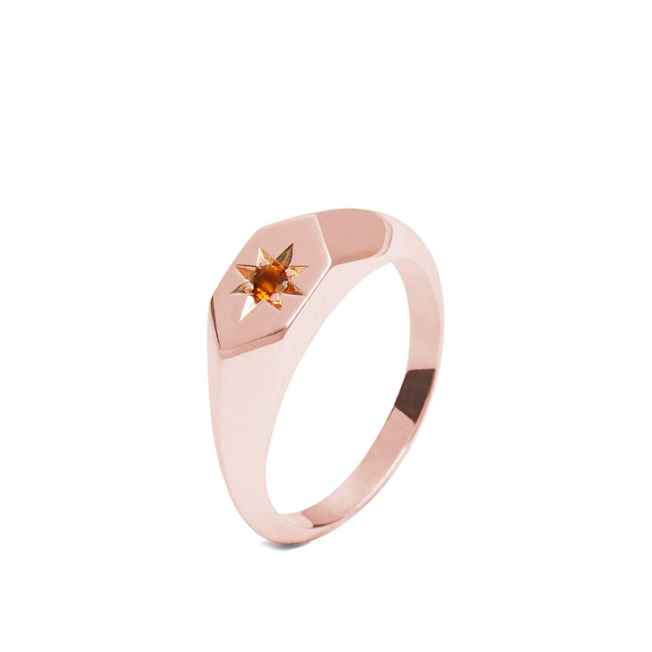 A rose gold ring with a sleek, hexagonal face featuring an orange citrine gemstone set in a star-shaped setting. Handmade in Dublin, the band is smooth and thin, complementing the minimalist yet elegant design of the Starlight Palmeria Citrine Birthstone 9ct Gold Signet Ring by Cosmic Boulevard.