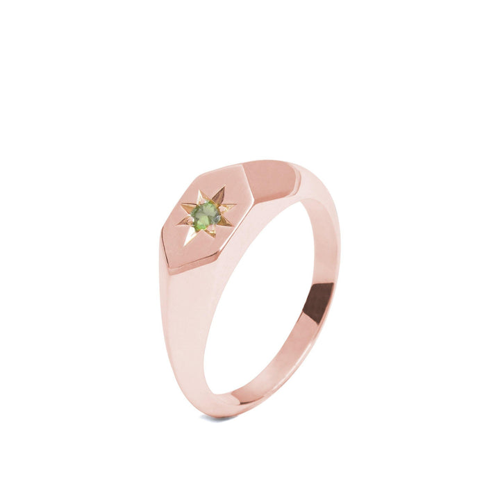 A sleek rose gold, handmade-in-Dublin ring with a minimalist design. The band has a smooth finish, thickening slightly at the top where a small star-shaped setting holds a single, pale green gemstone. This Starlight Peridot Birthstone 9ct Gold Signet Ring by Cosmic Boulevard boasts modernity and elegance.