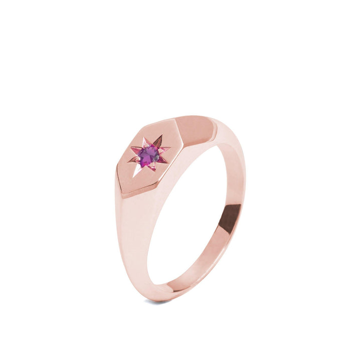 A Starlight Pink Tourmaline Birthstone 9ct Gold Signet Ring by Cosmic Boulevard features a small pink tourmaline shaped like a star and set into an octagonal bezel on its top. The band is smooth and polished, with a simple yet elegant design.