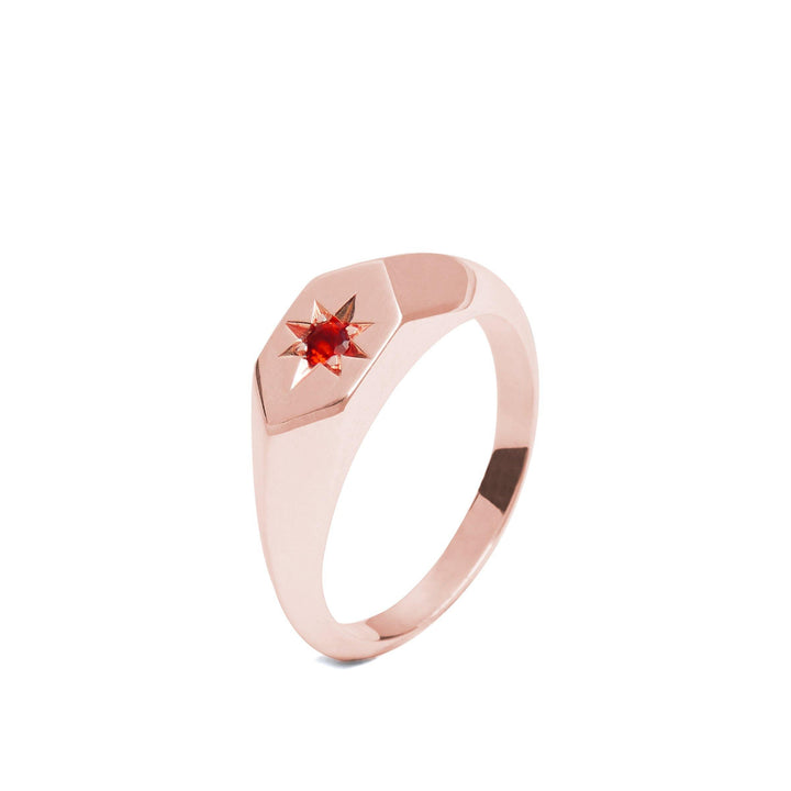 A Starlight Mozambique Garnet Birthstone 9ct Gold Signet Ring by Cosmic Boulevard featuring a small, bright red garnet set in a star-shaped design at the center. Handmade in Dublin, this piece boasts a sleek, smooth band and a modern, minimalist aesthetic.