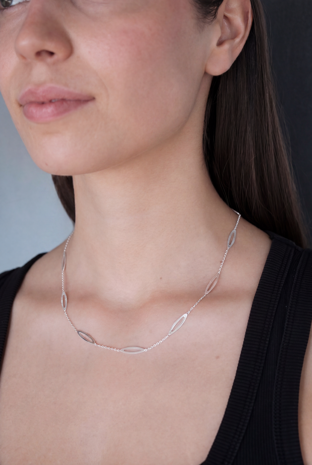 A woman wearing a black top and the Tezer Leaf Chain Necklace—a delicate sterling silver piece featuring oval-shaped links—shown from the shoulders up against a neutral background.