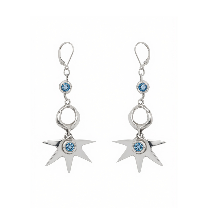 Réalta Earrings with 2 moissanite by Madeleine Blaine showcase circular and irregular silver forms adorned with blue gemstones, culminating in a striking starburst motif. Handcrafted to reflect the elegance of luxury jewelry, these earrings are beautifully presented against a white background.