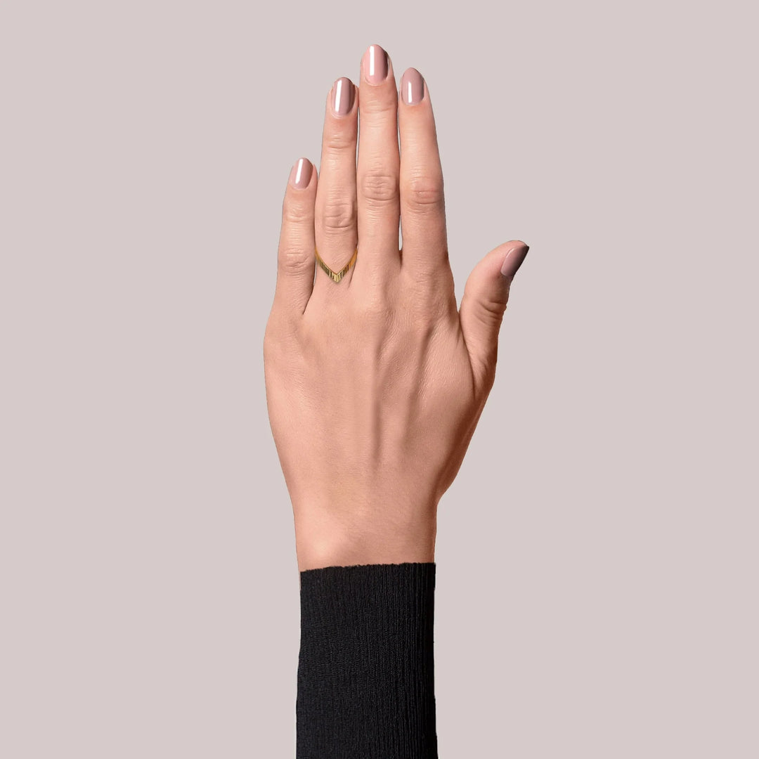 A hand with neatly manicured nude nails wears the Jane Koenig Reflection V ring on the ring finger, paired with a black long-sleeve top against a plain light gray background.