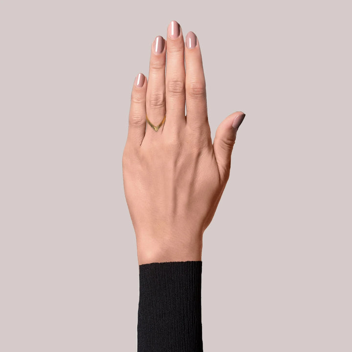 A hand with neatly manicured nude nails wears the Jane Koenig Reflection V ring on the ring finger, paired with a black long-sleeve top against a plain light gray background.