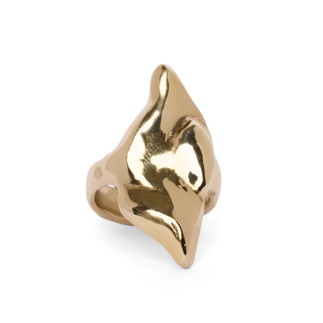 The Rift Ring by Madeleine Blaine is showcased against a white background, featuring a bold, abstract, and sculptural design with smooth curved surfaces and pointed edges. This striking gold jewelry piece artfully incorporates negative space, creating an eye-catching effect that distinguishes it from the ordinary.