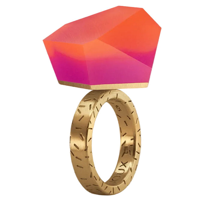 The Fruit Bijoux Ring Top VU Crystals Sunset Pink by Fruit Bijoux showcases a large, geometric gemstone in vivid pink and orange hues, accented with engraved markings for a bold, modern style.