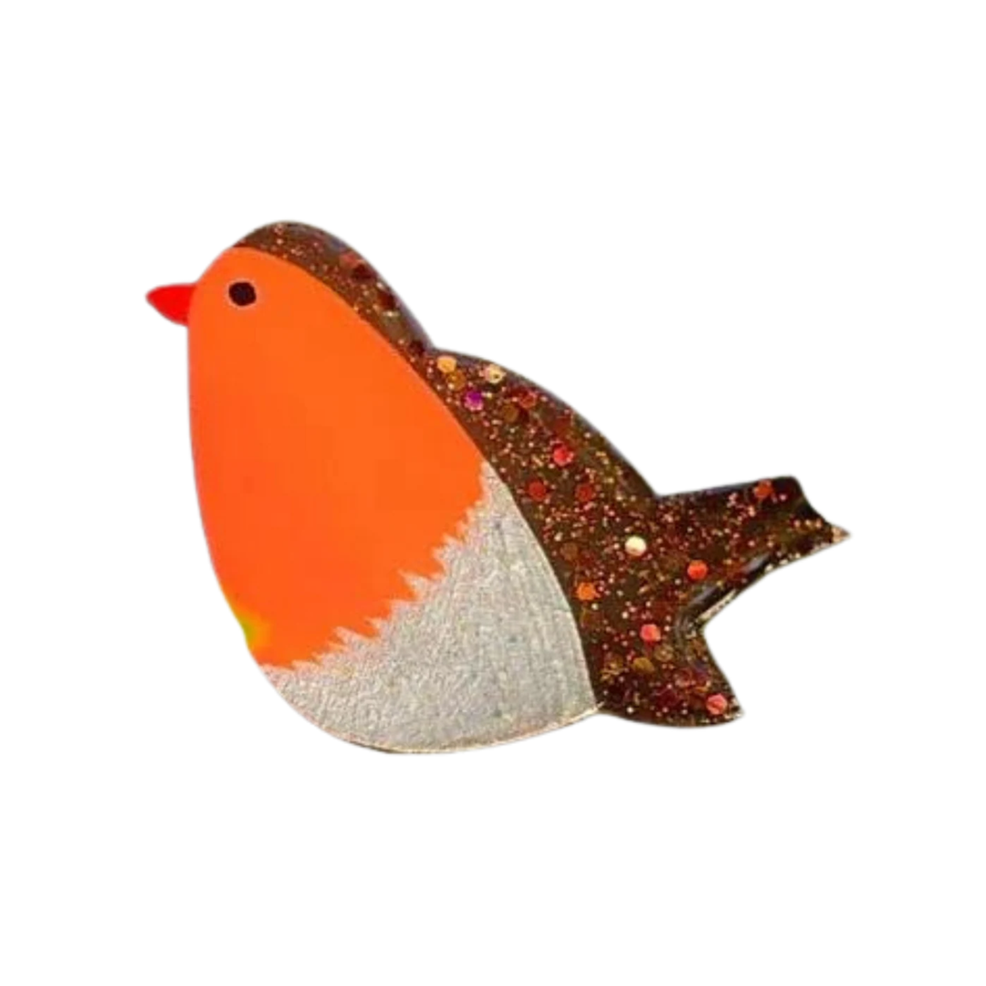 The Naoi Robin Pin Brooch is a handpainted wooden accessory featuring an orange body, white belly, black eye, red beak, brown wing and tail with colorful glitter accents, finished in smooth resin.