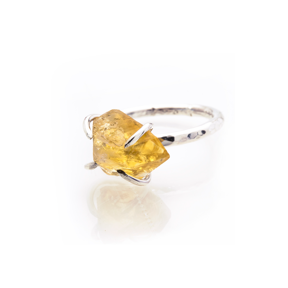 A Caroline Stokesberry-lee Citrine Rock Ring featuring a large, rough-cut Raw Citrine stone at its center. The irregular shape of the stone is held in place by four prongs, adding a unique and naturalistic aesthetic to the jewelry piece. The ring is photographed against a plain white background.