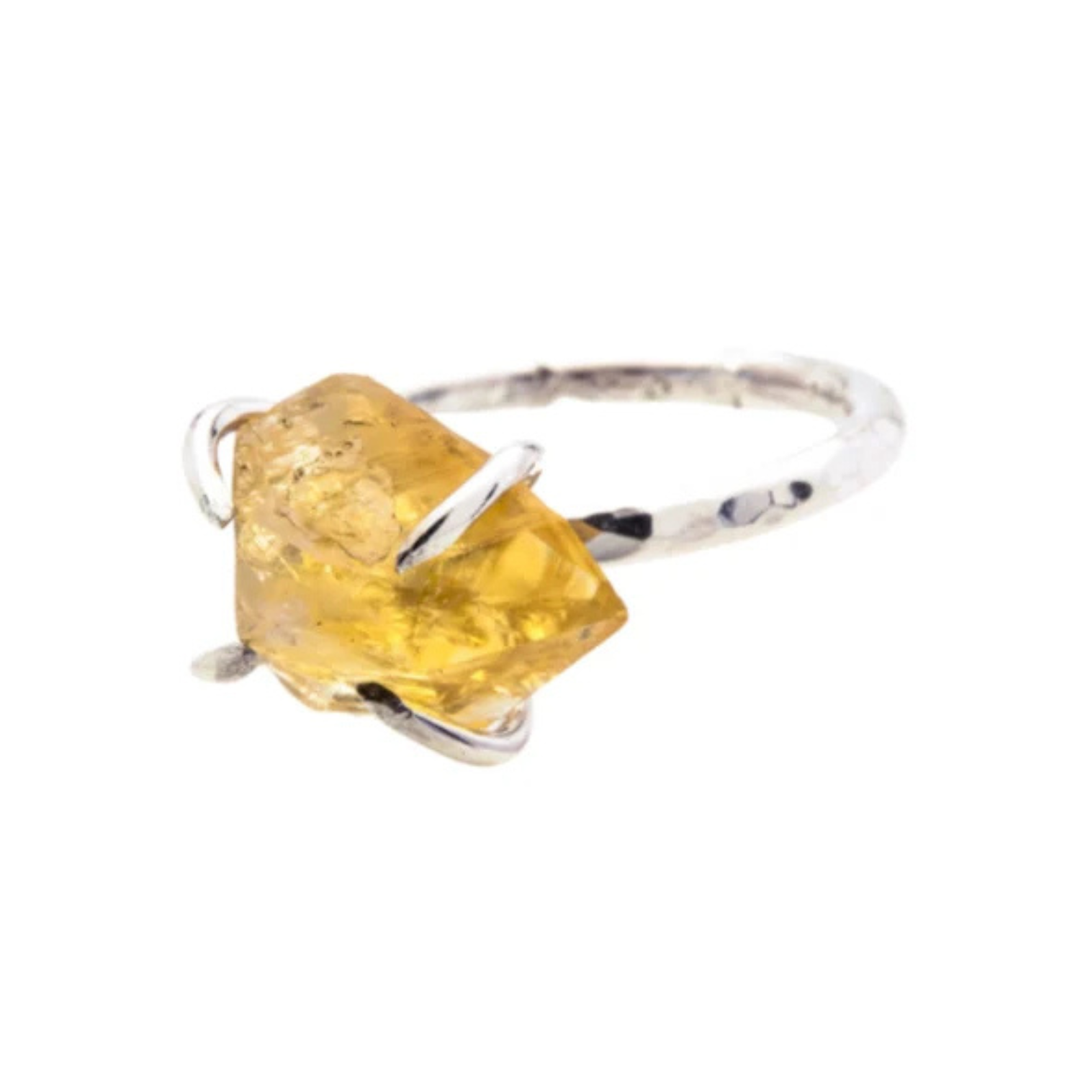The Caroline Stokesberry-lee Citrine Rock Ring features a raw Citrine gemstone set in an irregular, natural shape. The gemstone is held in place by delicate prongs, showcasing its natural facets. The ring band is slim and polished, highlighting the bright, raw beauty of the stone.
