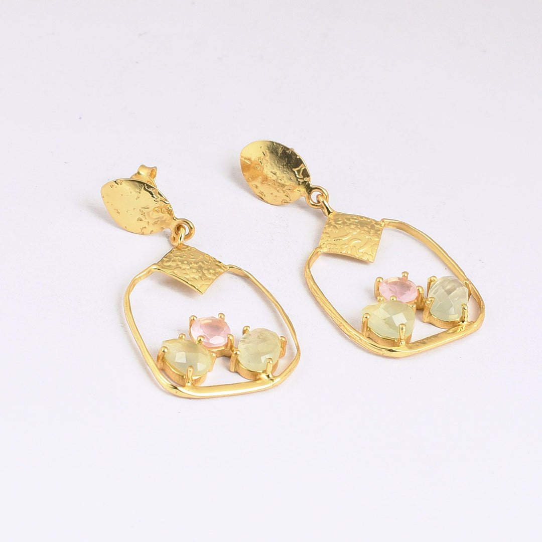 A pair of Watermelon tropical Rose Chalcedony & Rainbow Moonstone Square Gold Earrings features irregular, textured oval hoops. Each earring is adorned with three faceted gemstones in pastel shades of pink, green, and yellow, set towards the bottom of the hoops. The earrings have gold, hammered stud posts.