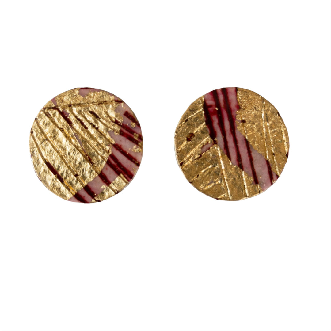 Introducing the Rothlú Ró Sgraffito Stud Earrings in Red/Black: a sophisticated pair of round earrings showcasing a blend of gold-textured and maroon diagonally striped designs. These exquisite pieces are securely fastened with sterling silver posts, elegantly displayed against a plain white background.