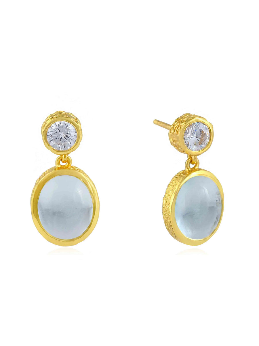 A pair of elegant Serena Earrings by Shyla featuring round, clear gemstones in 22 carat gold settings at the top, and larger, semi-translucent pale blue gemstones encased in hand hammered gold settings suspended below. The earrings have a simple yet sophisticated design.