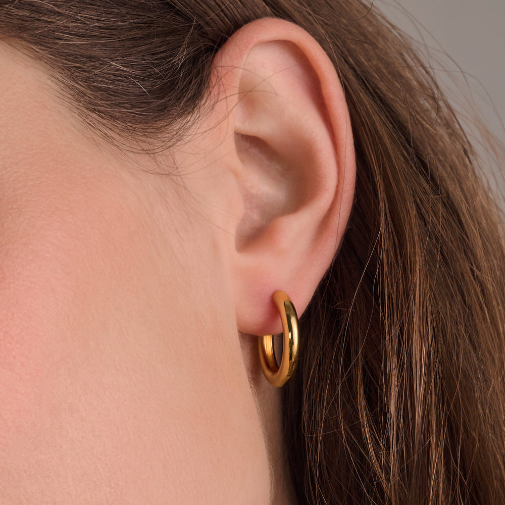 Close-up of a woman's ear with straight brown hair, wearing a small, thick Sif Jacobs Carrara Pianura gold plated hoop earring.