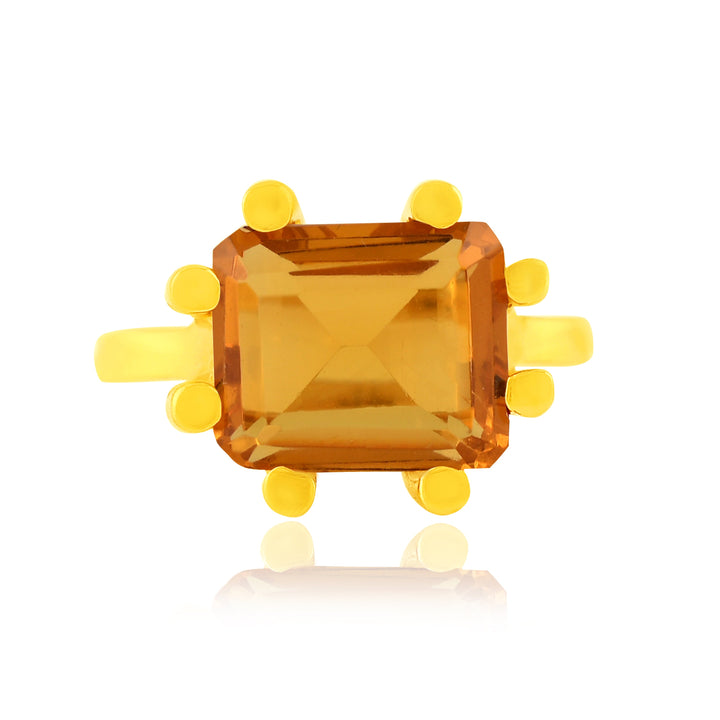 A Square Claw Gold Plated Ring by Shyla featuring a rectangular, amber-colored gemstone in the center, held in place by six prongs. The 22 carat gold band is smooth and polished. The gemstone reflects light, highlighting its faceted surface. The ring is displayed against a white background.