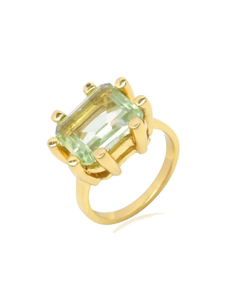 A chunky ring features a large, rectangular light green gemstone secured by prongs. The gem is prominently set above a plain 22 carat gold band, displaying a modern and elegant design. This is the Square Claw Gold Plated Ring by Shyla.