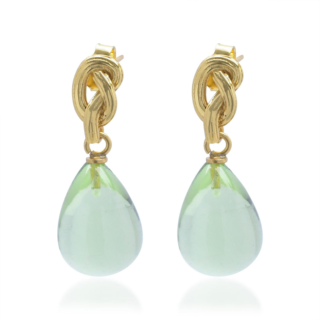 The Shyla Synthea Earrings in various colours feature an intricate gold knot top with a large, translucent light green teardrop gemstone gracefully dangling below. Hypoallergenic for sensitive ears.