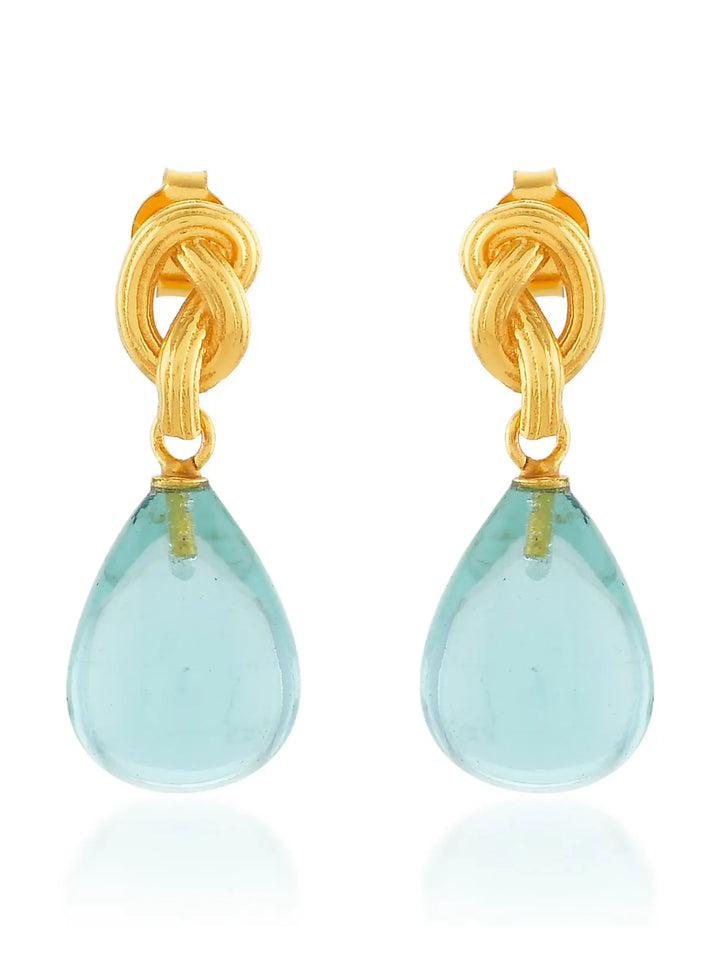 The Synthea Earrings by Shyla feature gold knots with teardrop light blue gemstones, shown on a white background. These hypoallergenic earrings offer stylish, everyday elegance and are perfect for sensitive ears. Available in various colours.
