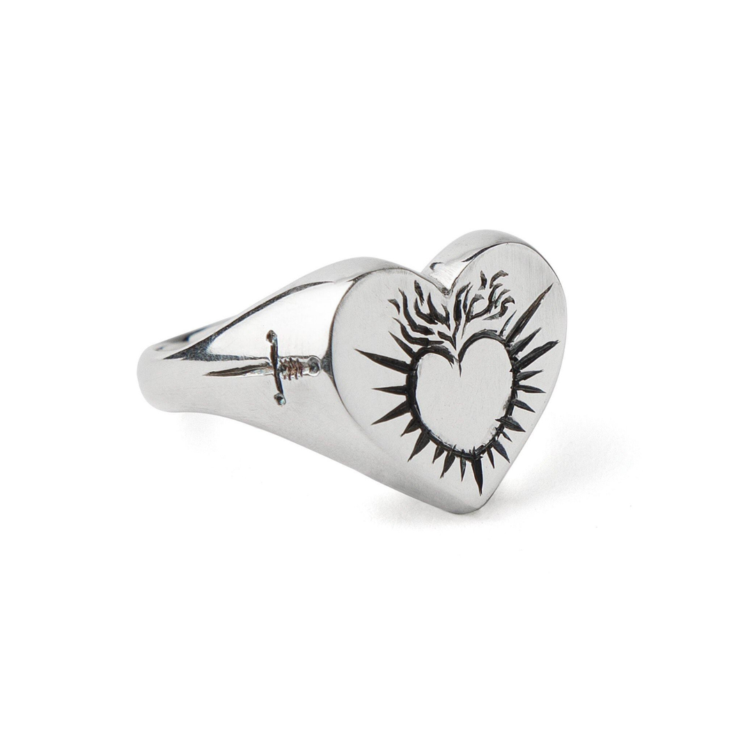 The Sacred Heart Signet Ring by Cosmic Boulevard is a hand-engraved sterling silver ring with a flame-accented heart face and a small dagger etched along the band.