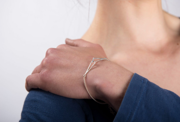 A person in a blue long-sleeve top rests their hand on their shoulder, showcasing the Miriam Wade Le Chéile Bracelet Silver on their wrist against a plain light background.