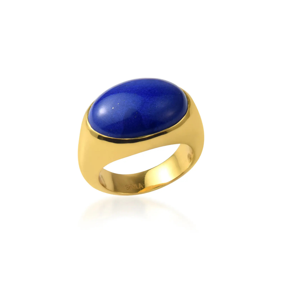 The Shyla Serifos Ring features a chunky gold band and a large deep blue oval stone, making it a striking statement accessory, shown against a white background.