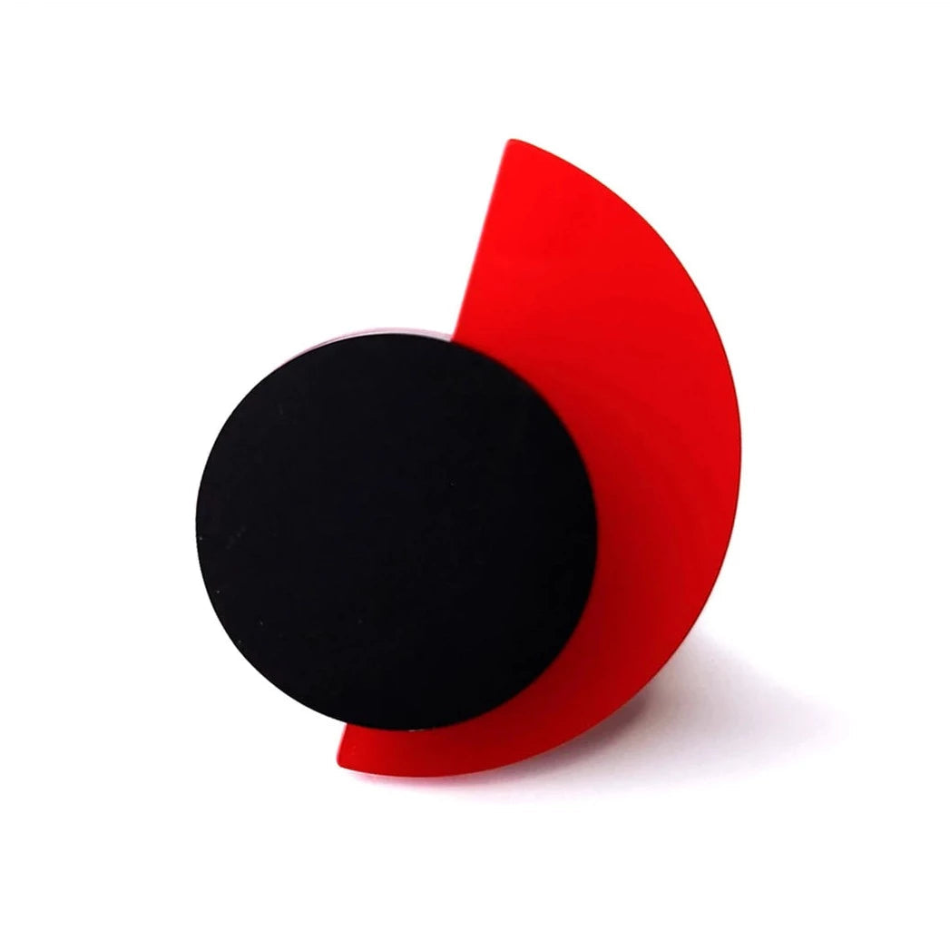 A modern, abstract sculpture featuring a flat black circle positioned against a red crescent shape. The red crescent extends slightly beyond the perimeter of the black circle, creating a striking contrast between the two geometric forms, much like an avant-garde Suzan Ring from Alex + Svet.