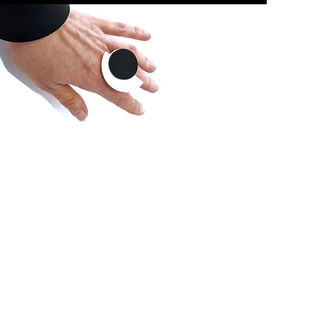 Close-up of a hand wearing a large, round, black and white Suzan Ring by Alex + Svet. The hand is positioned against a plain white background, with the ring prominently displayed. Crafted in a Paris studio, the person is wearing black clothing that is partially visible in the top left corner of the image.