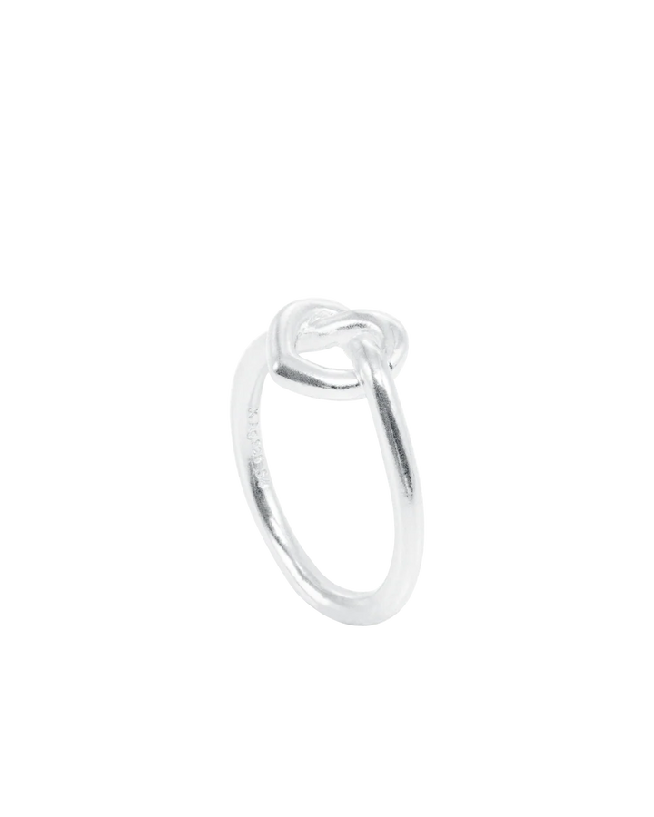 The Jane Koenig Tied Heart Ring is a sterling silver piece with a knot design, shown against a white background.