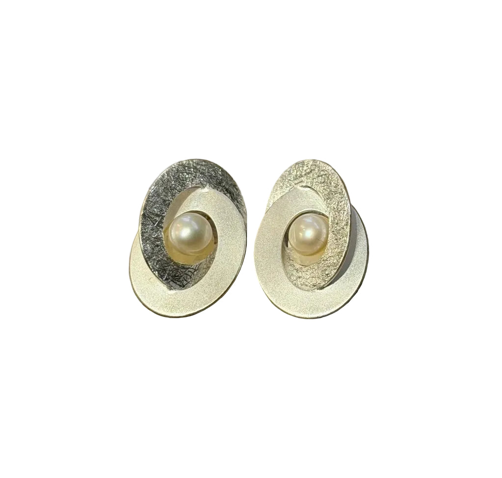 Tezer's Silver Overlapping Circle Earrings with Freshwater Pearl feature oval-shaped, textured sterling silver layers and a luminous pearl at the center, shown on a white background.