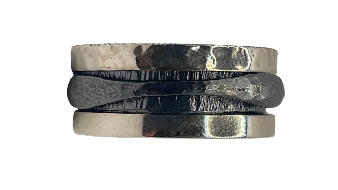 The Oxidised single spinner ring by K.And is a wide, silver-toned piece with a hammered finish and a raised, wavy black band across the center, giving it a rugged, handcrafted look.