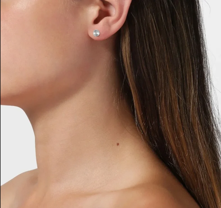 A close-up side profile of a woman wearing a small round silver stud earring against a white background.