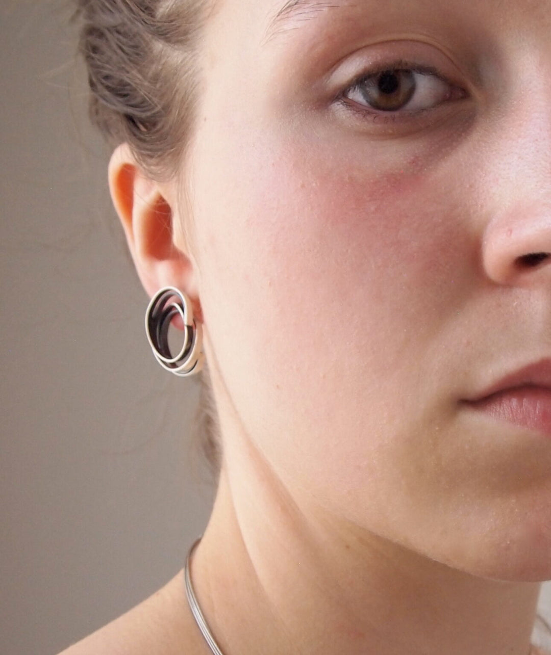 A close-up of a person with a circular earring in matte silver.  The earring they are wearing is the Small Mo Silver Earrings by MarCucurella.