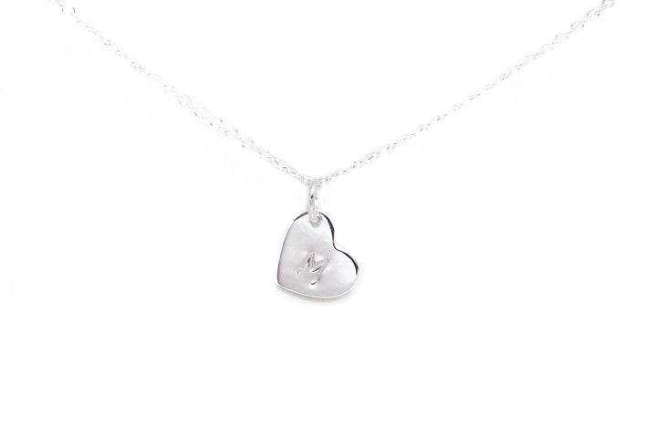 A delicate silver necklace featuring a small, heart-shaped pendant with the letter "M" engraved in the center. The **Personalised Small Heart Charm in Silver** by **Personalised Charms** boasts an oval belcher chain and a secure lobster claw fastening. The image is set against a plain white background.