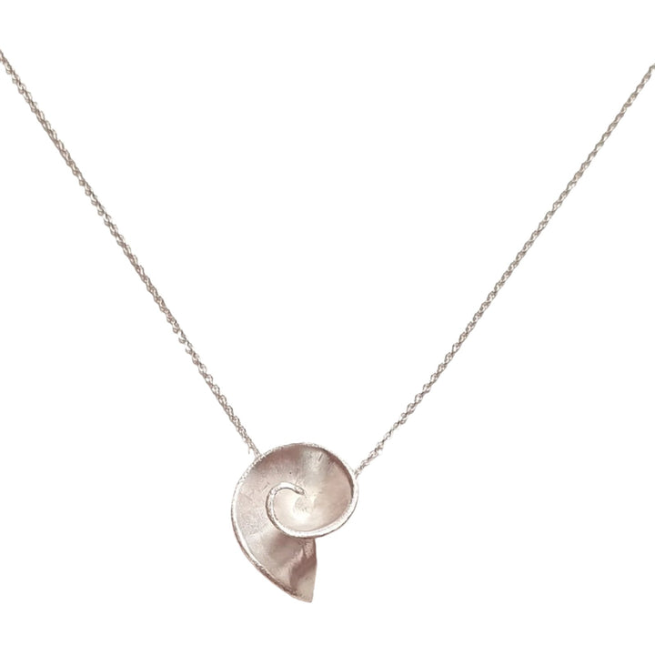 A delicate sterling silver necklace features the Small Swirl Pendant by Georgia Charal, hanging from a fine, slender chain. The background is a plain, light-colored surface.