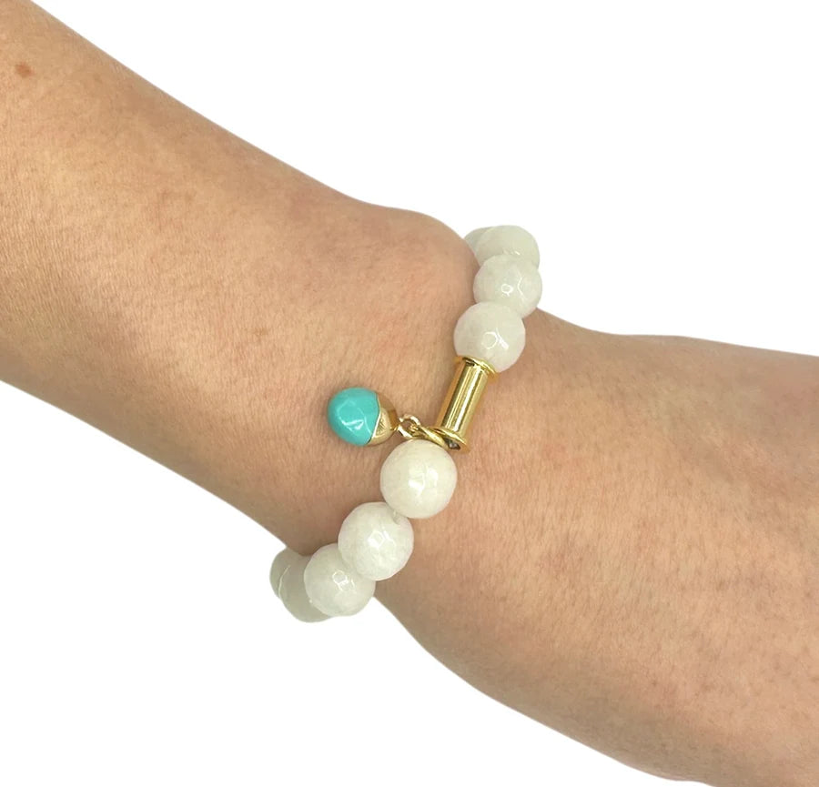 A hand wears the Aria V Soulstone White Agate and Turquoise Bracelet, handmade in Dublin with large round white agate beads, a gold accent, and a single turquoise charm.