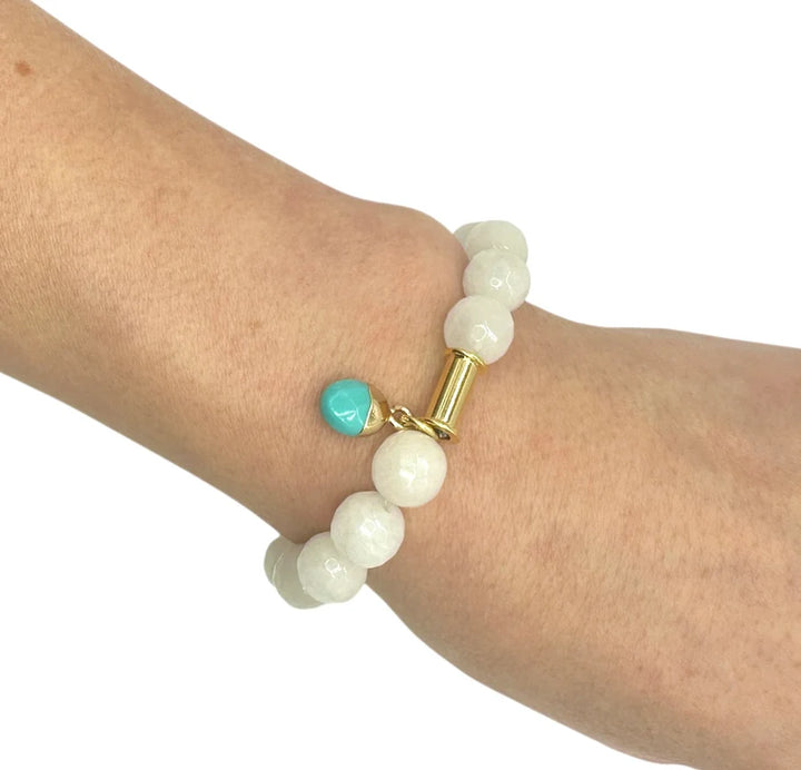 A hand wears the Aria V Soulstone White Agate and Turquoise Bracelet, handmade in Dublin with large round white agate beads, a gold accent, and a single turquoise charm.