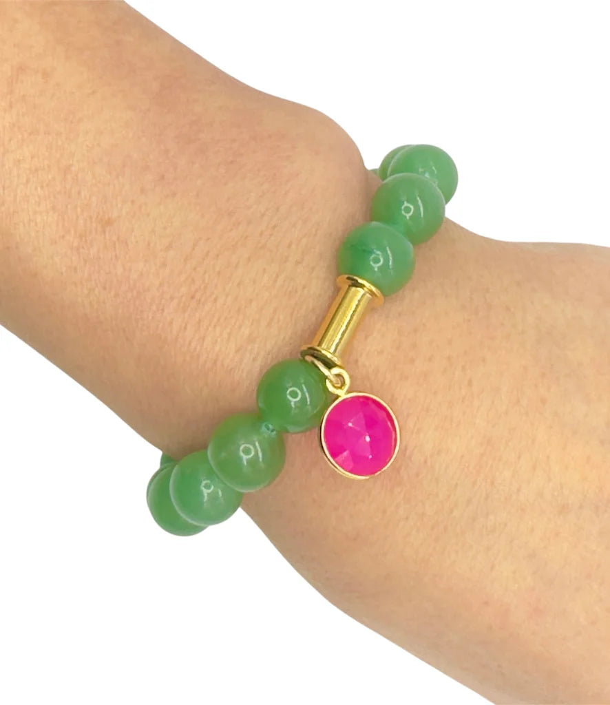 A wrist dons the Aria V Soulstone Moss Agate and Pink Chalcedony Bracelet, handmade in Dublin, featuring green beads, a gold cylindrical accent, and a small round pink charm.