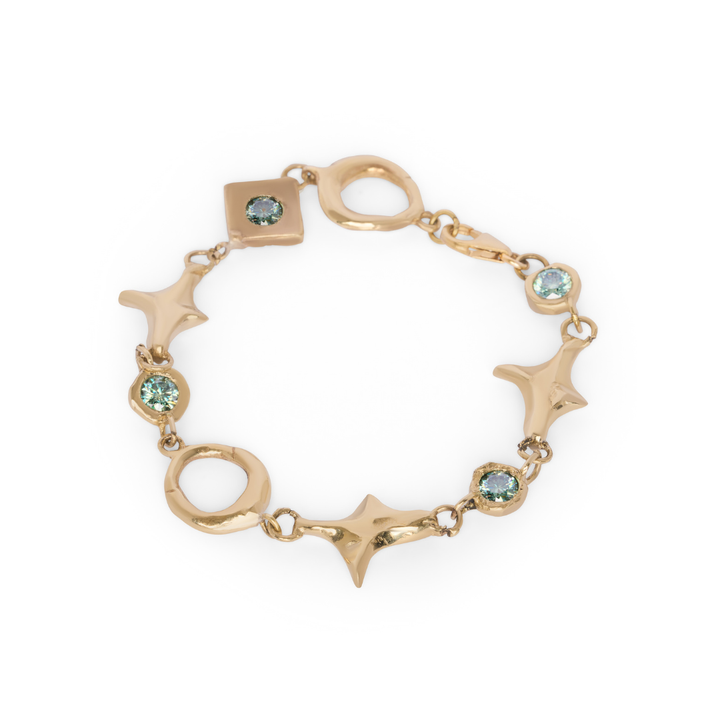 Introducing the Spark Bracelet by Madeleine Blaine: expertly crafted in gold with alternating star, circle, and square links, each highlighted by a light blue gemstone—this elegant piece symbolizes energy and connections, showcased beautifully against a white backdrop.