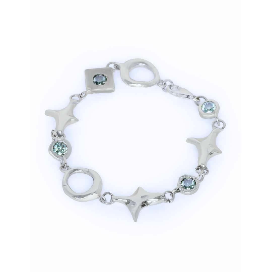 Introducing the Madeleine Blaine Spark Bracelet, showcased on a white background. This elegant silver bracelet features round, square, and star-shaped links adorned with delicate light blue gemstones. Its distinctive design celebrates unique connections and positive energy.