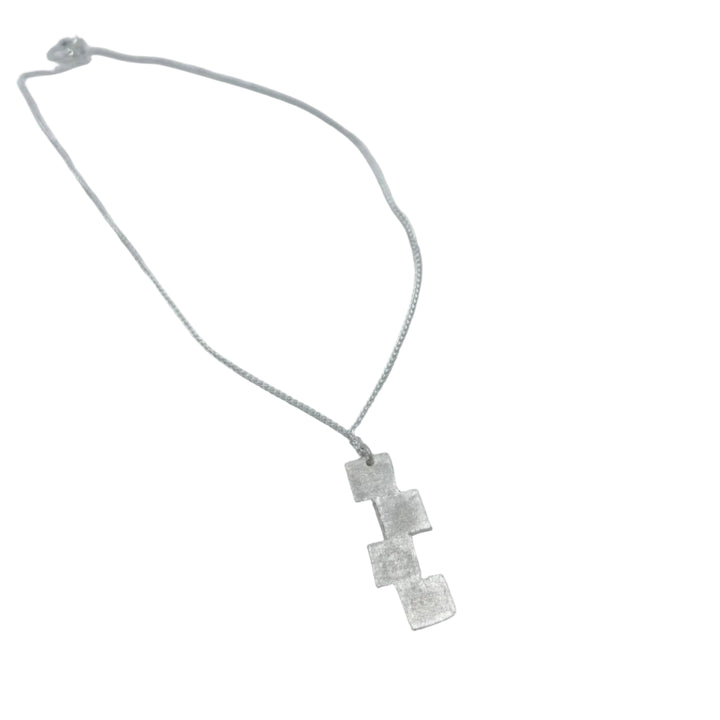 The Stairway to Heaven Pendant by Soufana Attia features a delicate silver chain and an asymmetrical trio of textured square charms, evoking modern elegance, shown on a light gray background.