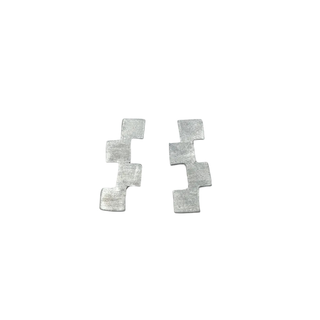 The Stairway to Heaven Earrings - Large by Soufana Attia are silver, matte-finished pieces featuring three connected squares in a zigzag, evoking modern asymmetry, displayed on a light gray background.