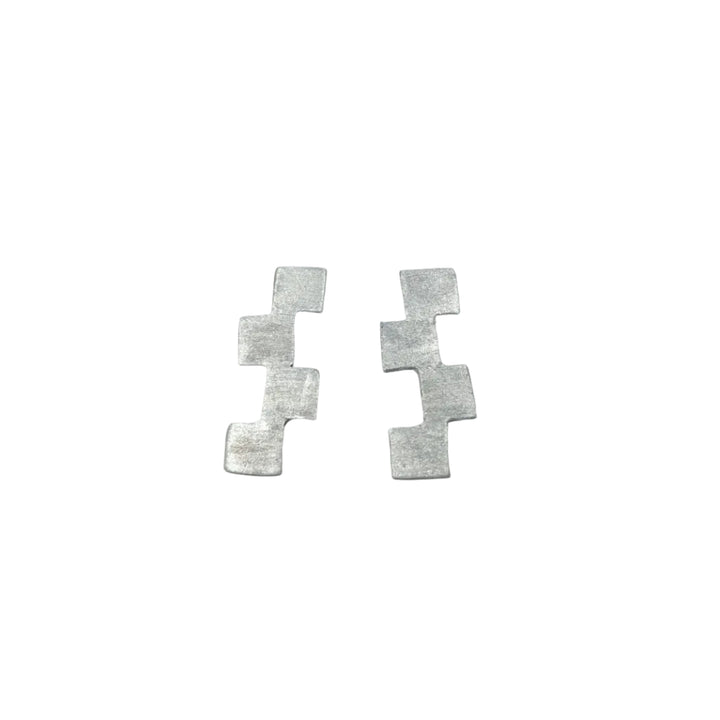 The Stairway to Heaven Earrings - Large by Soufana Attia are silver, matte-finished pieces featuring three connected squares in a zigzag, evoking modern asymmetry, displayed on a light gray background.
