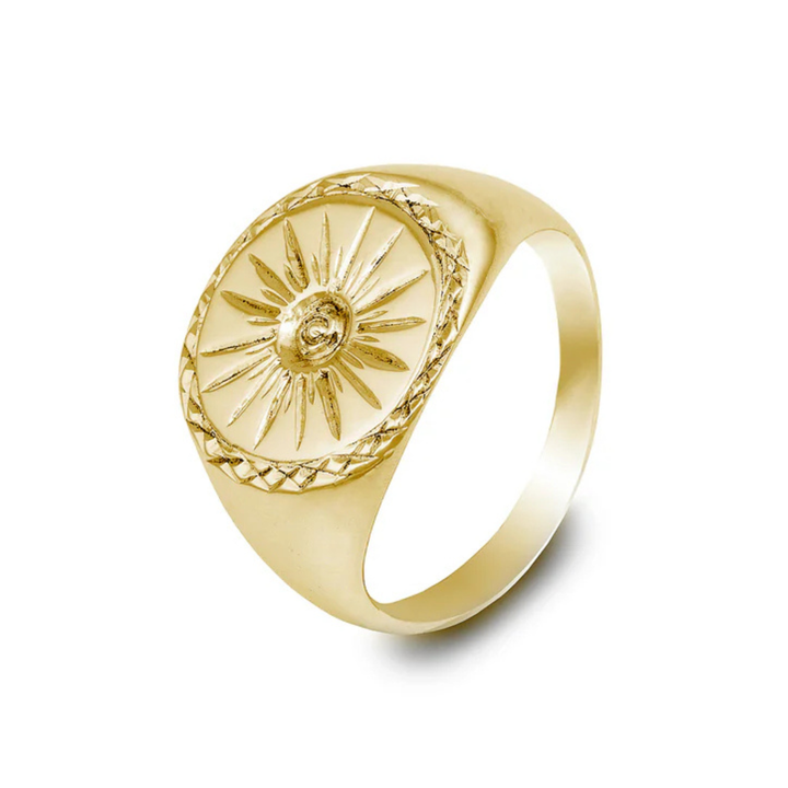 The Cosmic Boulevard Starburst 9ct Gold Signet Ring features an embossed sunburst design with a central engraved face. The band is smooth and polished, and the round face of this handmade signet ring has additional intricate detailing around the edge.