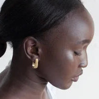 A dark-skinned woman with smooth features and pulled-back hair poses in profile with eyes closed, wearing Inner Island’s Strata Large Earrings, which add elegance against a simple, light background.