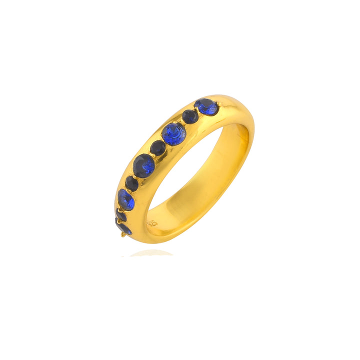 The Tasha Ring by Shyla, crafted from 22 carat gold, features seven evenly spaced blue gemstones. The shiny band has a smooth and polished finish, with the gemstones set in a single line along the top half. Displayed against a white background, this hypoallergenic jewelry piece radiates elegance and sophistication.